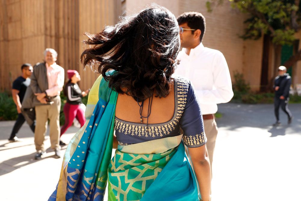 Woman in vibrant turquoise and blue sari walks past classical architecture columns.