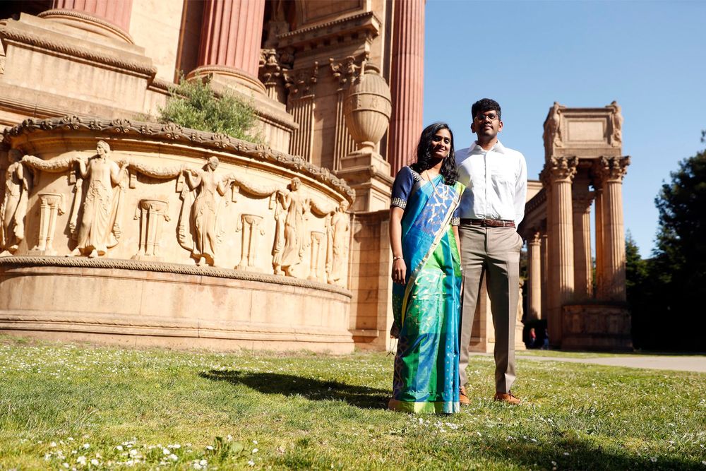 Traditional Indian couple stands near Palace of Fine Arts pillars and statues on a sunny day.