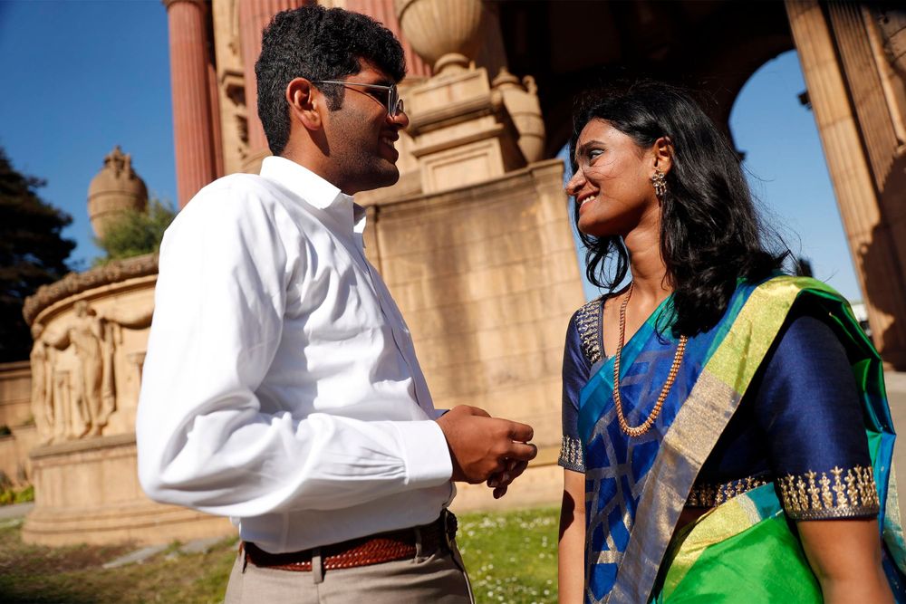 Elegant couple in formal attire shares intimate moment by historic columns during photoshoot.
