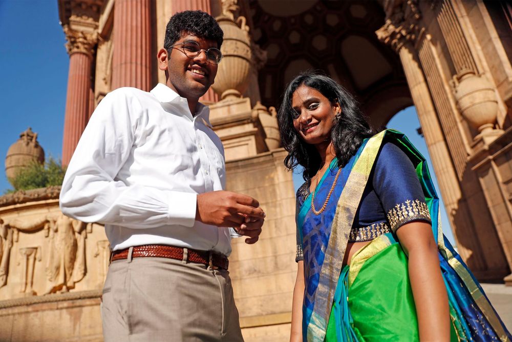 Couple poses near ornate architectural columns in formal attire with traditional Indian sari against terra cotta backdrop.