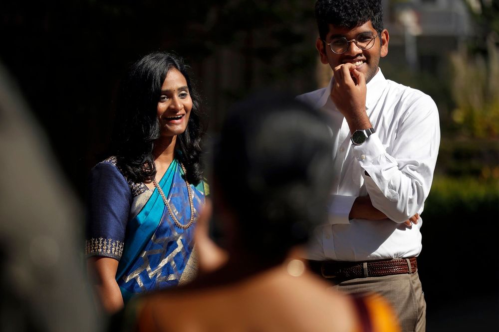 Couple laughs during outdoor photoshoot with photographer visible in foreground.