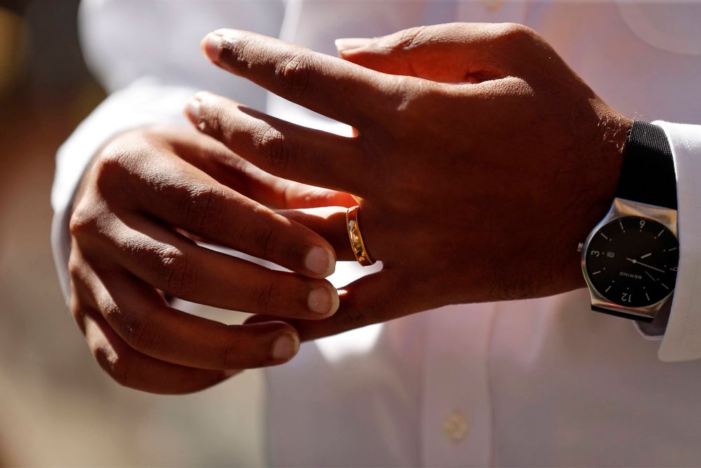 Close-up shot of hands exchanging a wedding ring in natural lighting.