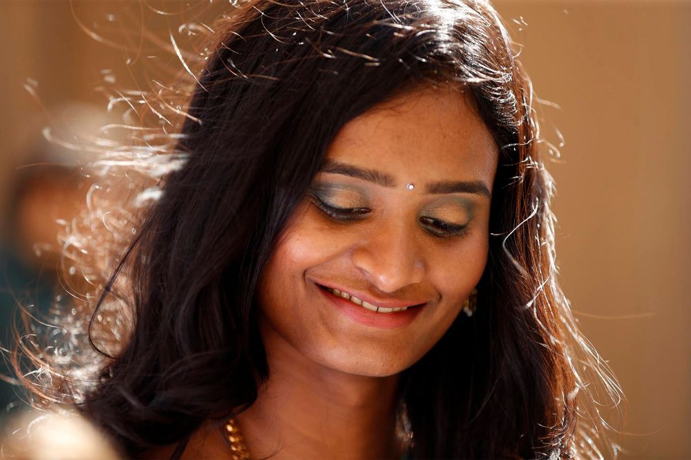 Woman with flowing hair smiles gently in warm sunlight wearing traditional jewelry.