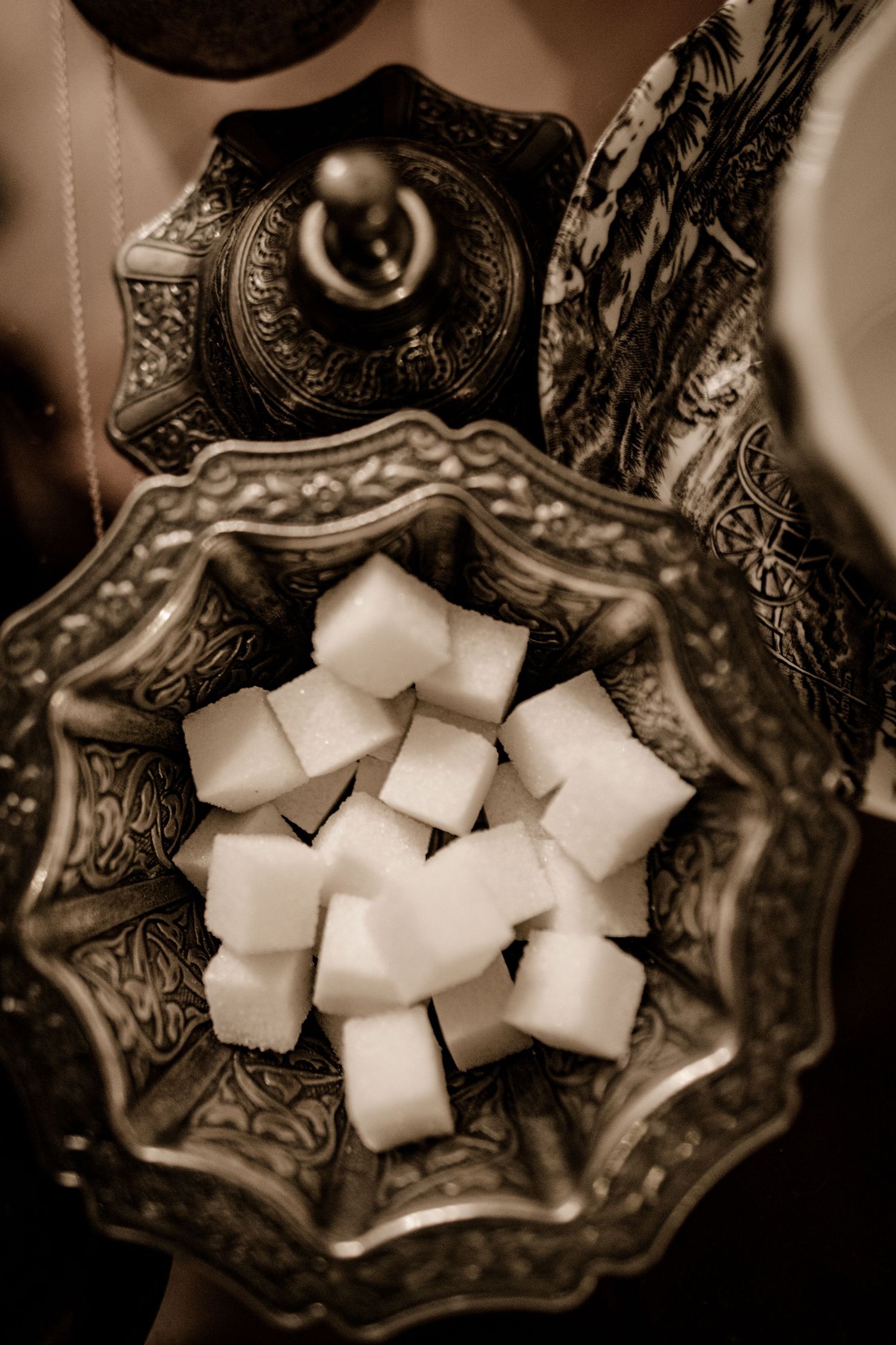 An ornate vintage dish filled with white sugar cubes in sepia tones.