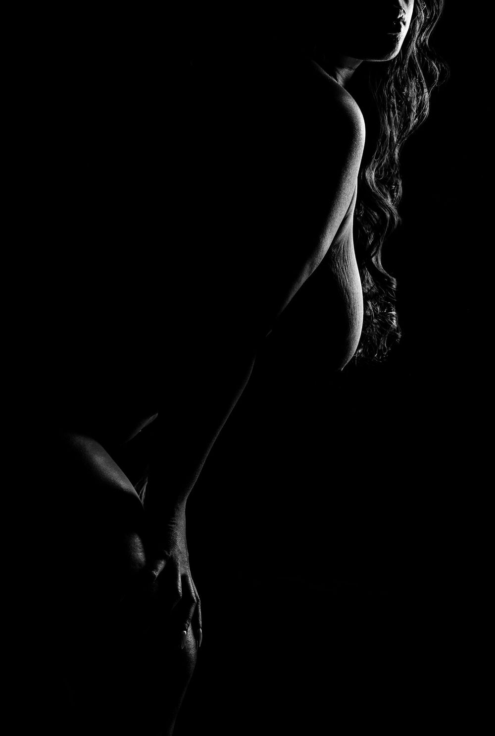Minimalist black and white silhouette showing feminine curves against dark background.