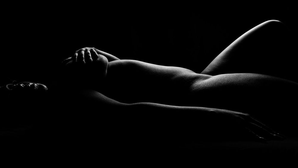Artistic black and white nude silhouette photograph showing graceful curves in dramatic low key lighting.