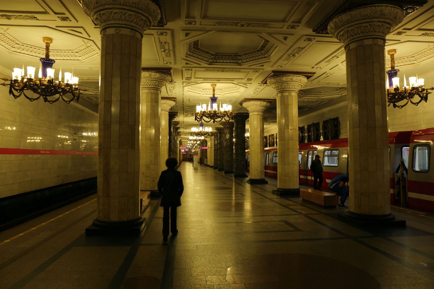 Dimly lit underground metro station platform with classical columns and chandeliers.