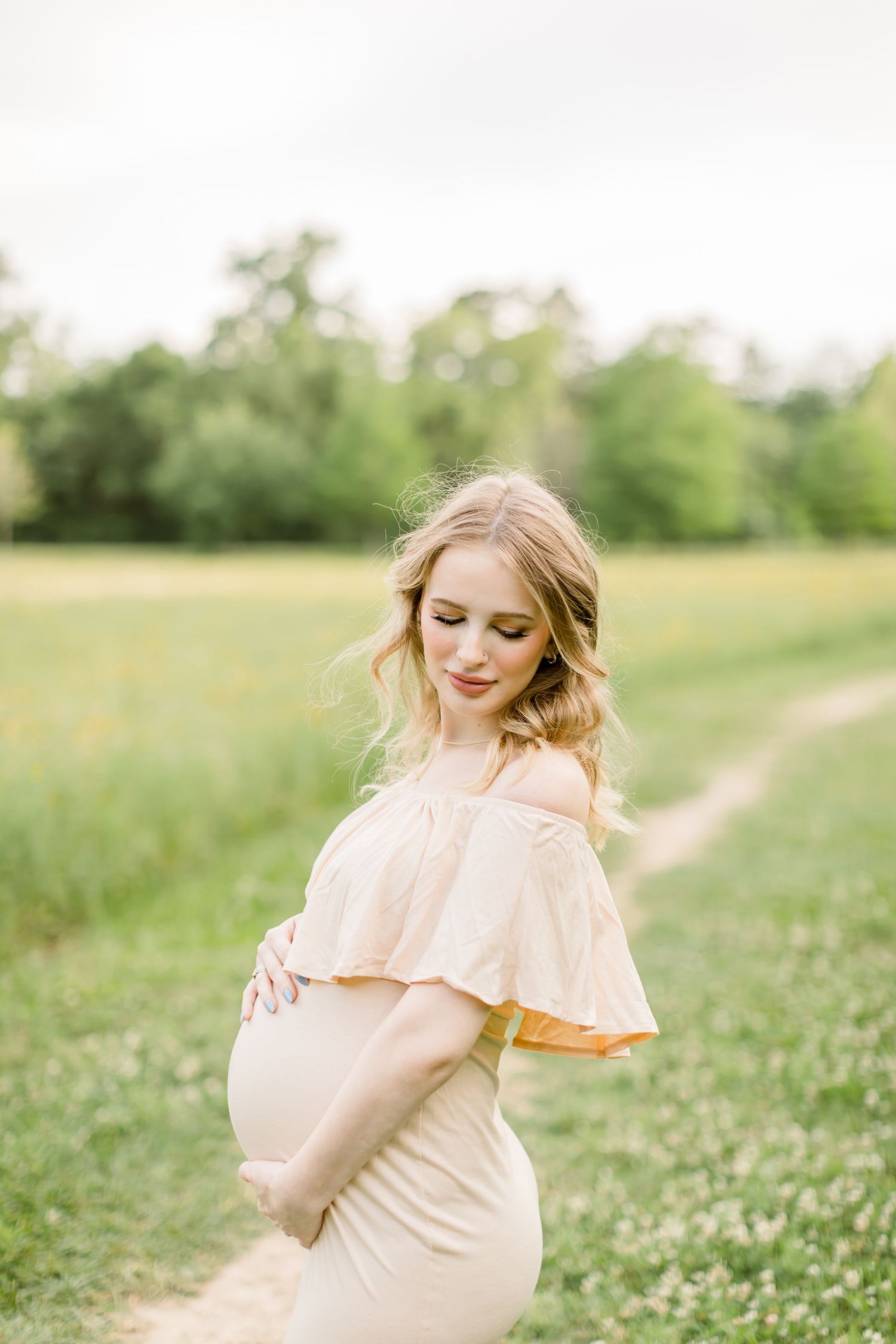 A delicate maternity moment captured in a flowing blush dress surrounded by spring flowers.