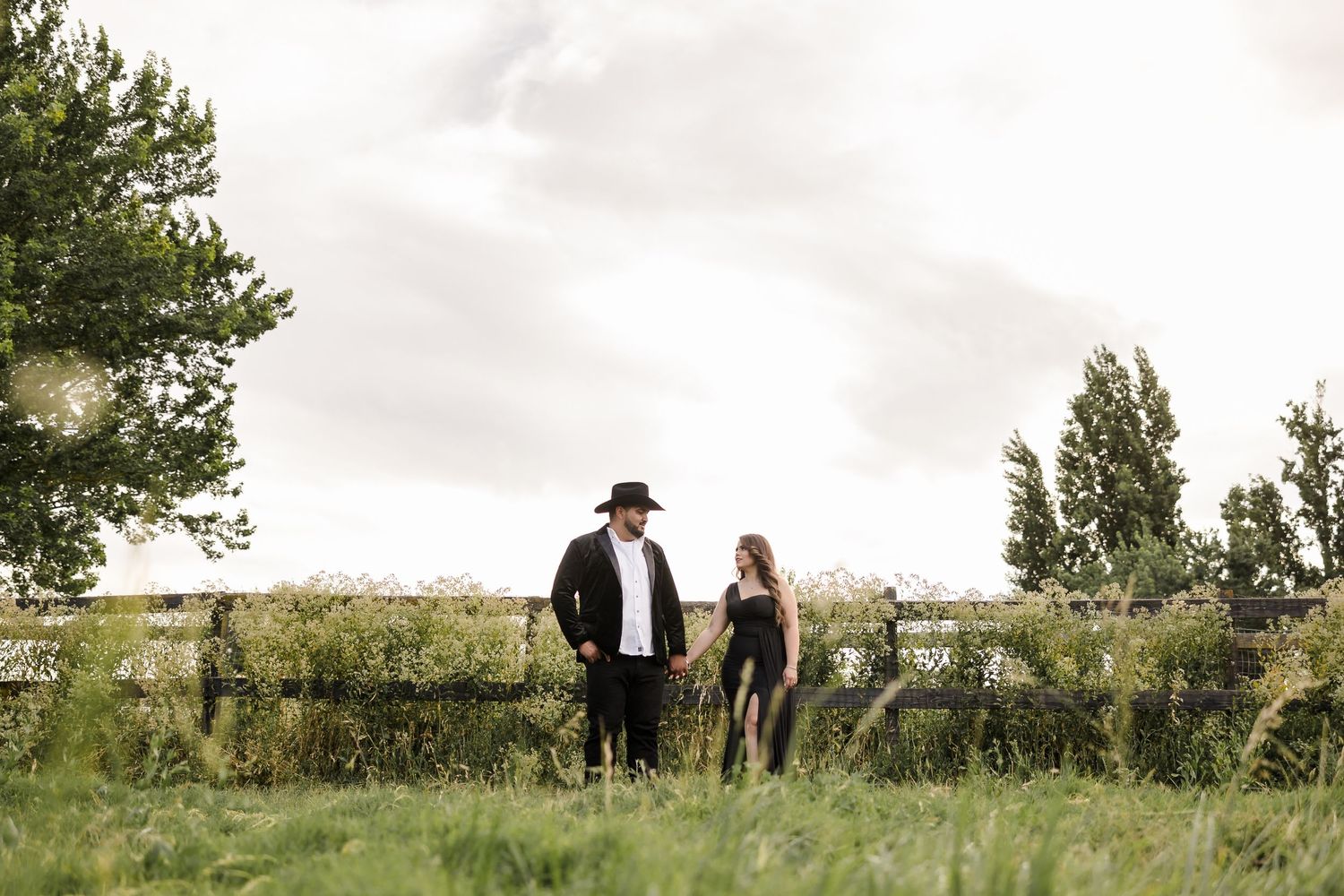 Couple standing together in a peaceful meadow with trees in the background.