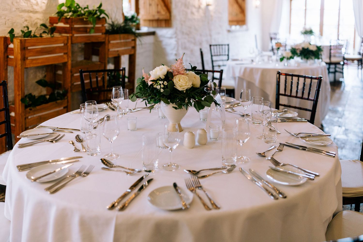 Round wedding reception table with white linens, formal place settings and a fresh floral centerpiece.