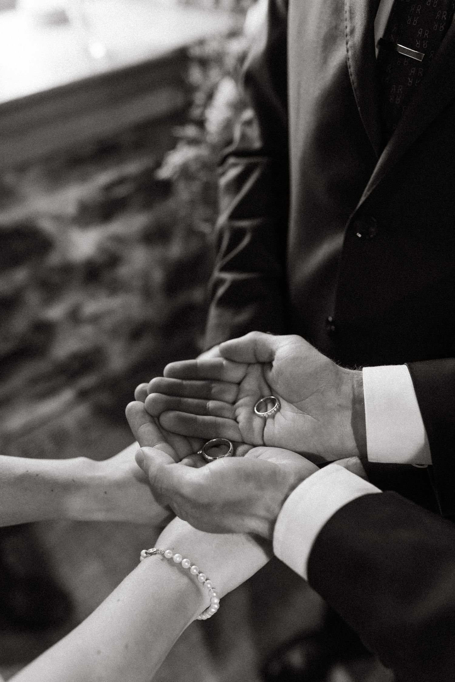 Black and white close-up of hands exchanging wedding rings during ceremony.
