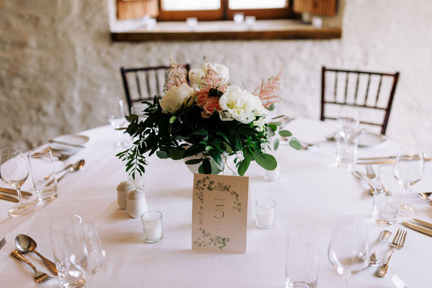 Elegant floral centerpiece with white and peach flowers on a white tablecloth at a formal wedding reception.