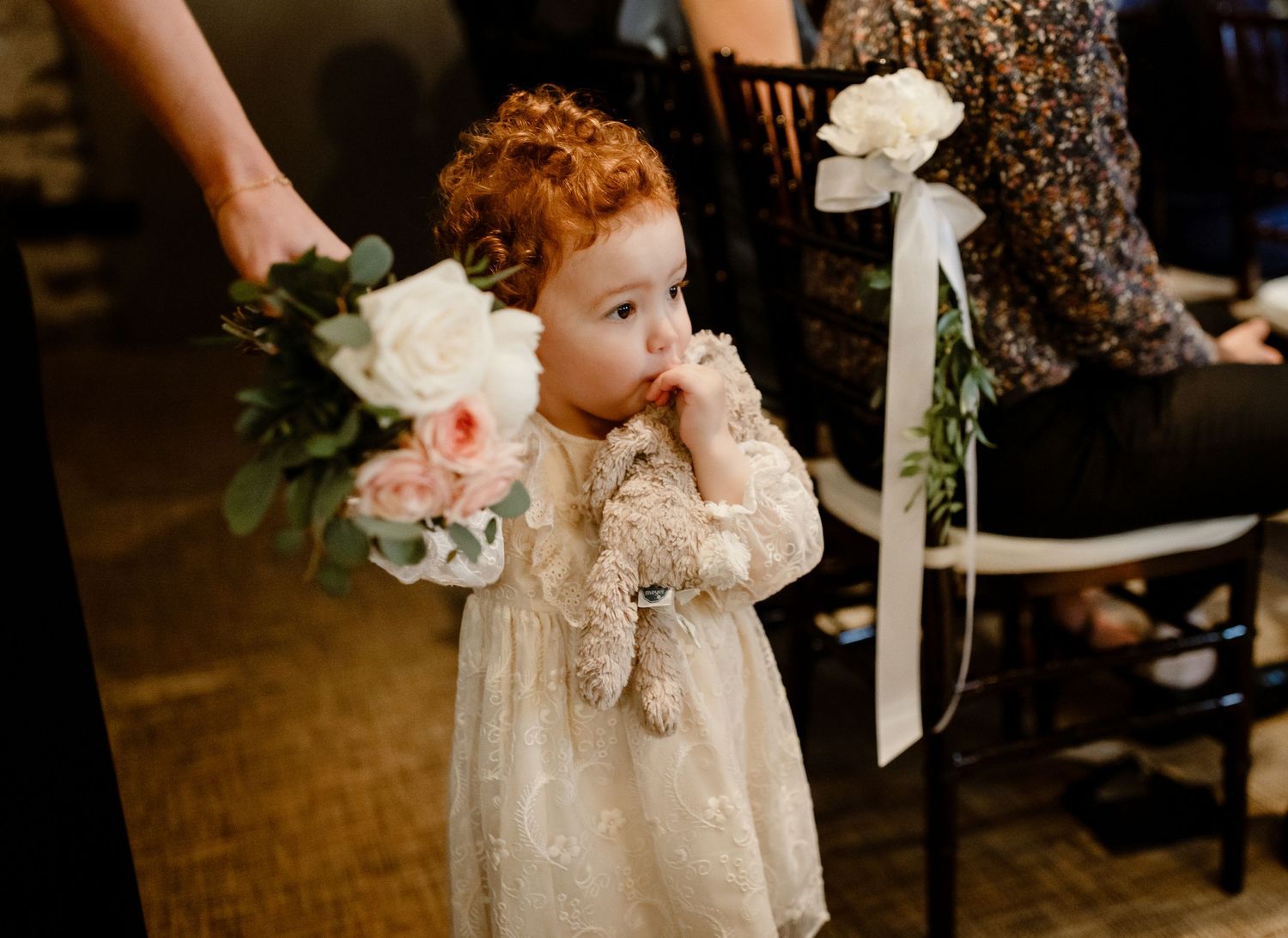 Young flower girl in sparkly dress holds bouquet during wedding ceremony.