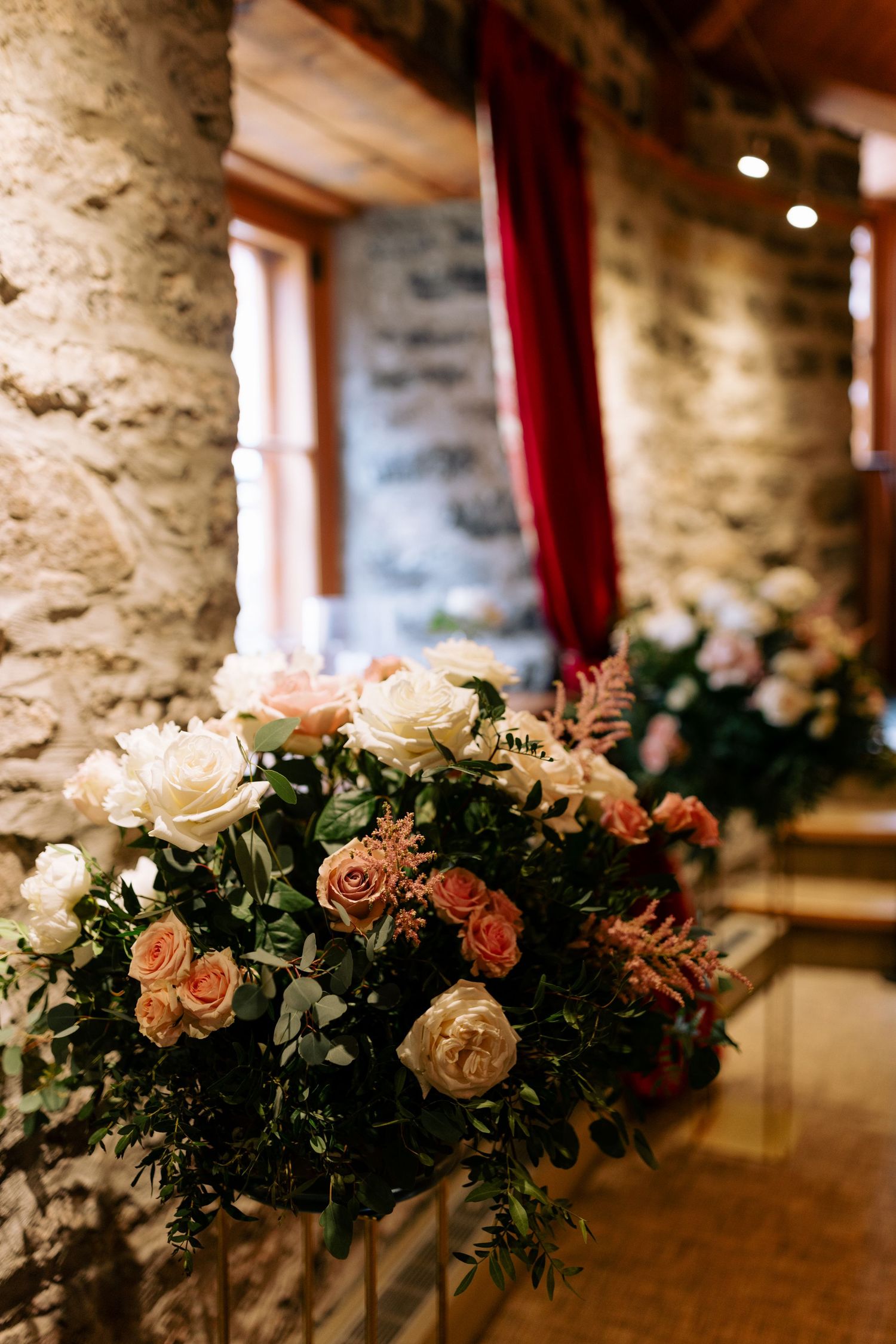 Lush floral arrangement with roses and greenery against a rustic stone wall.