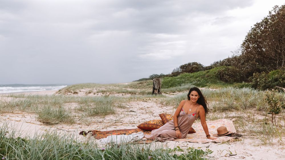 Woman in red bikini relaxing on sandy beach with dunes and stormy sky in background.
