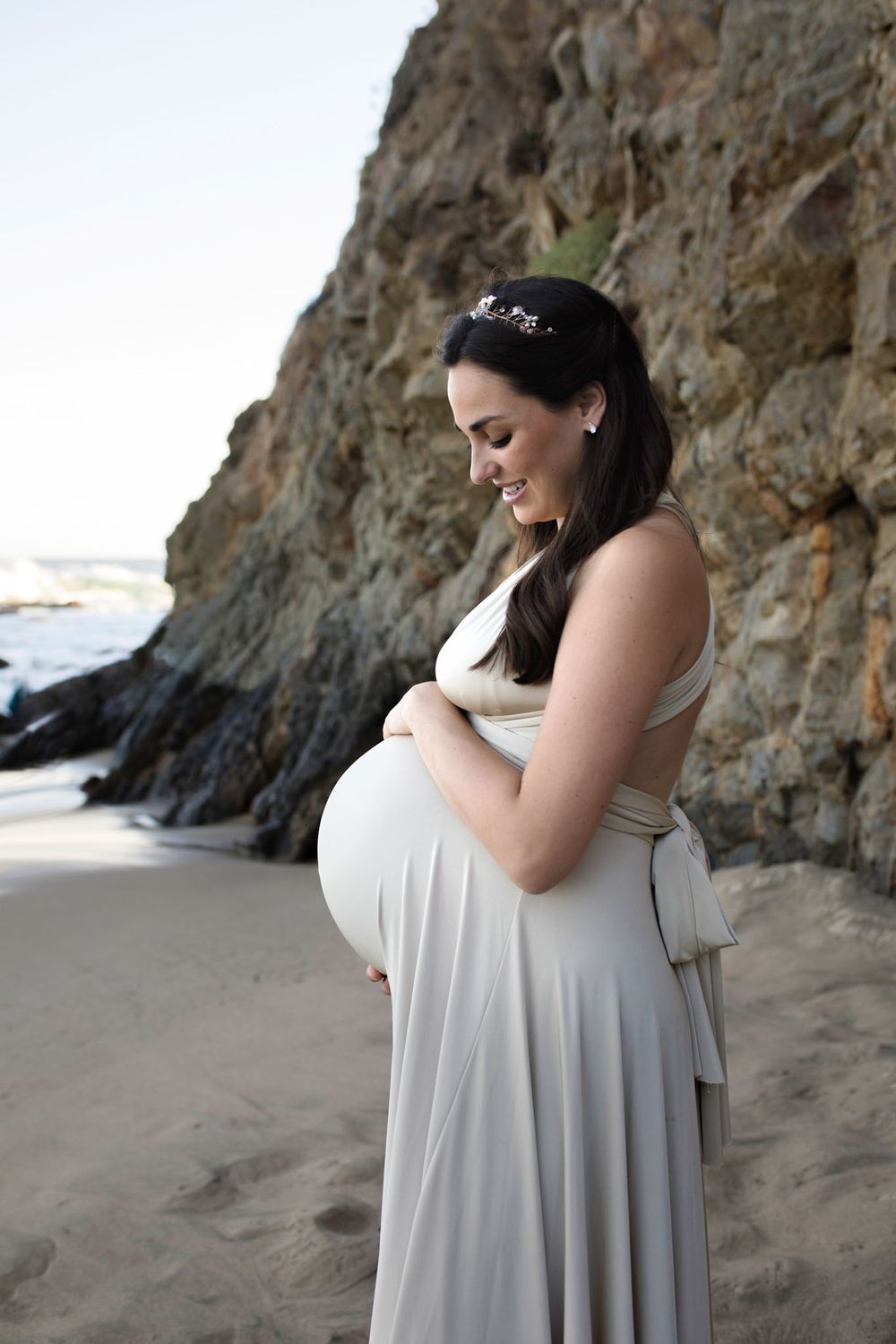 orange county maternity photographer - woman on the beach in a tan gown standing sideways holding her belly