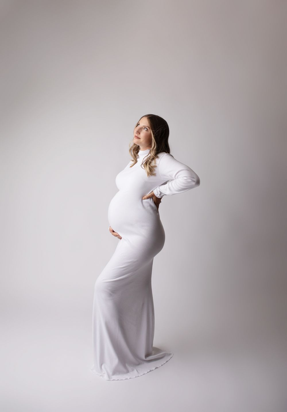 Orange county maternity photographer pregnant white mother wearing long white floor length long sleeve dress gazing up