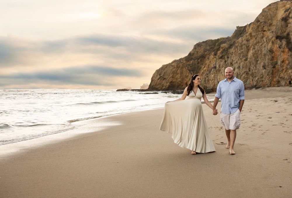 Orange county maternity photographer - pregnant mother holding her gown out holding her husbands hand walk on the beach