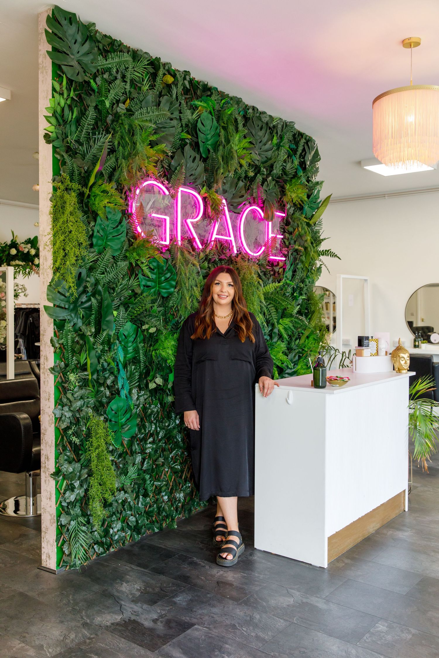 Modern salon interior with living plant wall and pink neon 'GRACE' sign during business branding photoshoot.