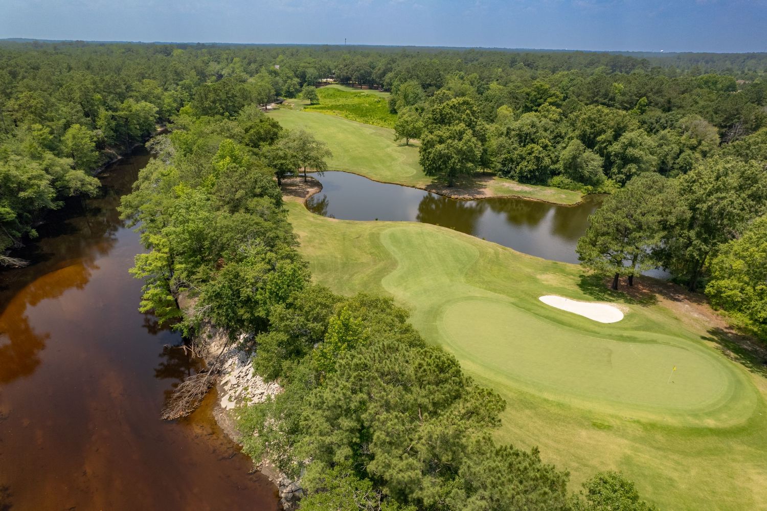 Golf course landscape featuring manicured greens, sand traps, and tree-lined fairways beside a river.