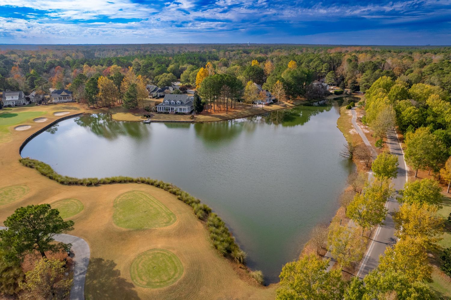 Drone shot of lakes and golf courses surrounded by autumn trees in a residential area.