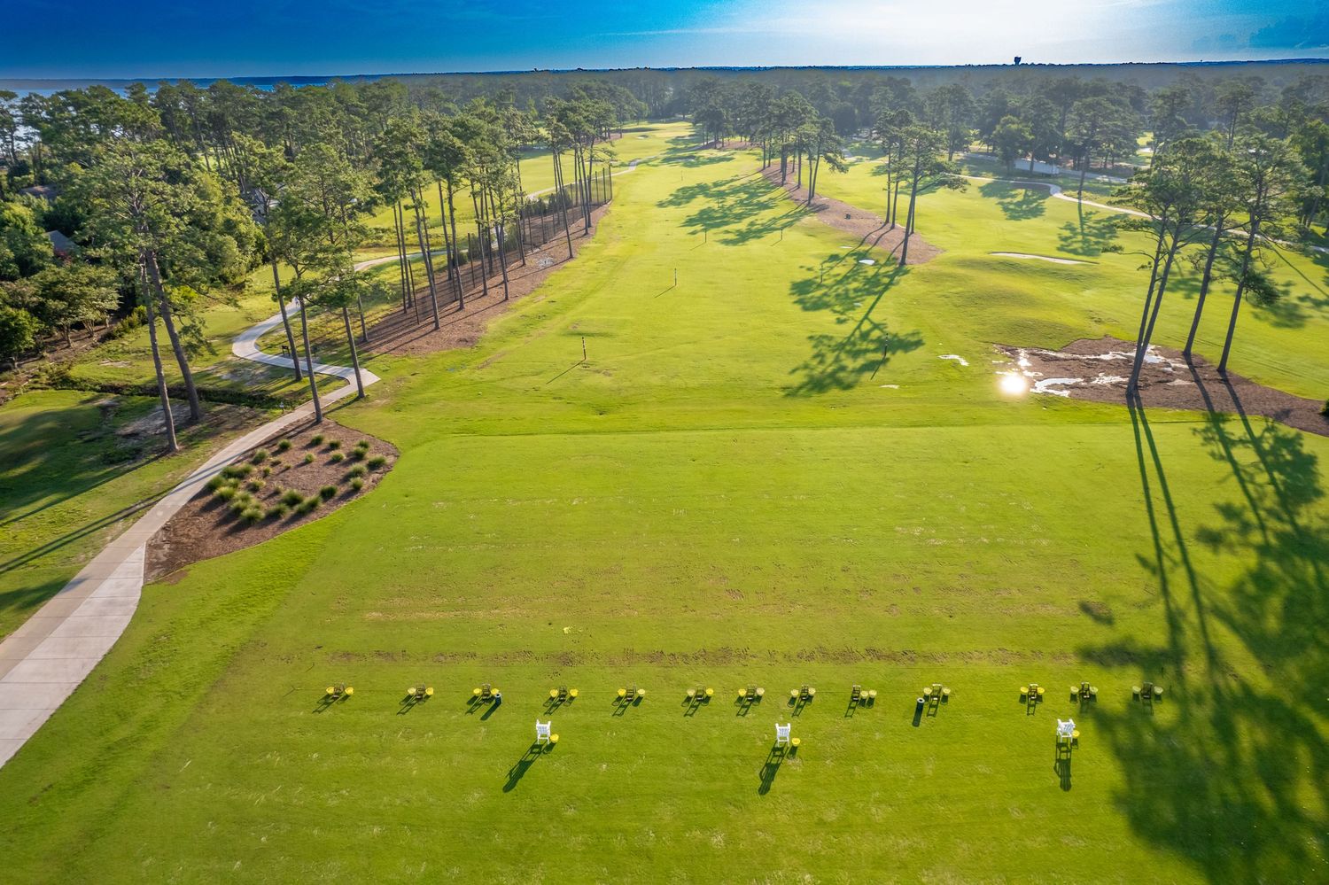 Aerial view of golfers and carts scattered across a lush green golf course surrounded by pine trees.