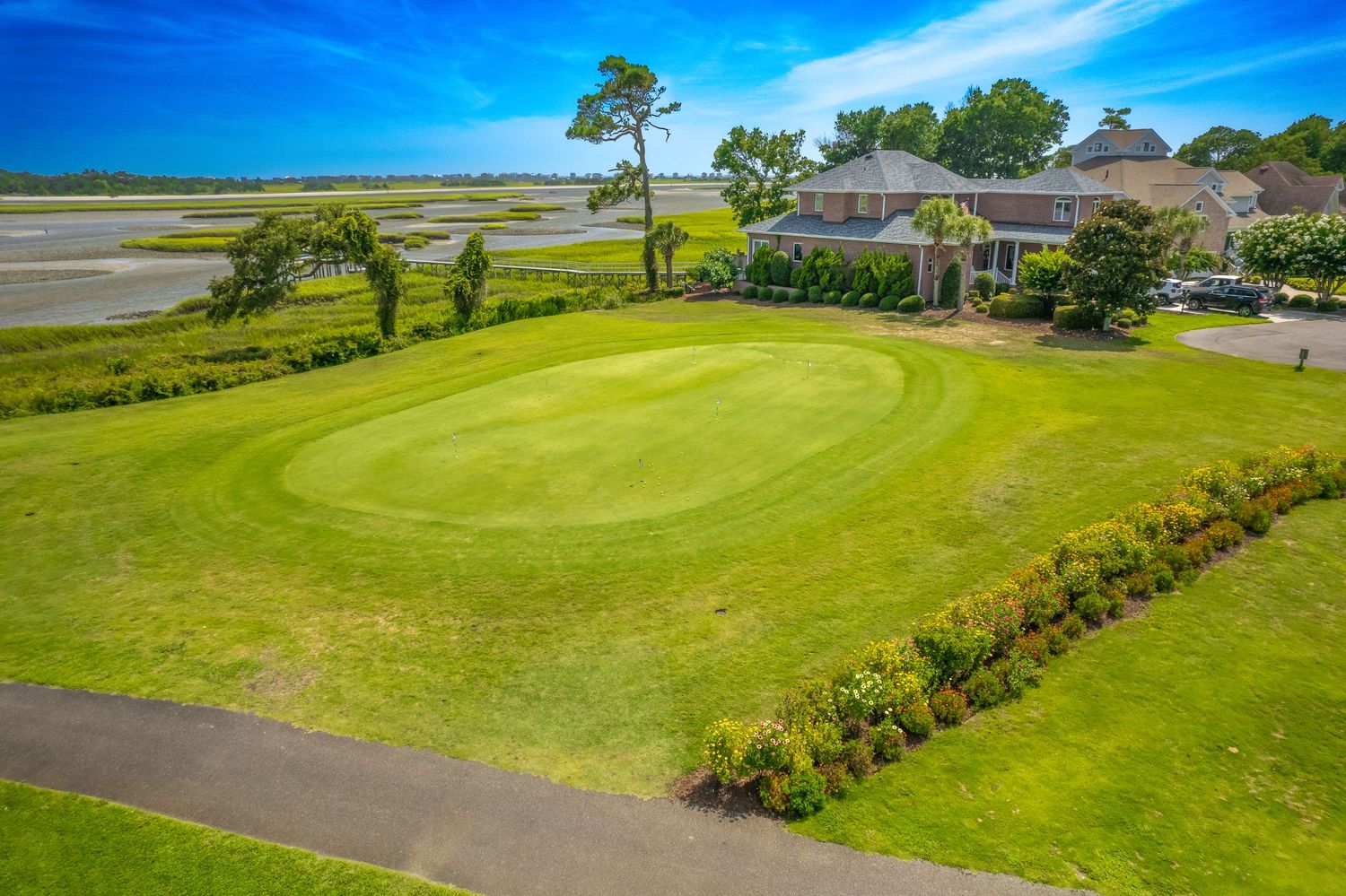 Aerial panoramic view of a coastal golf course with lush greens and fairways against a bright blue sky.