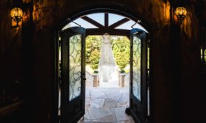 Wedding dress hangs in silhouette through arched doorway leading to outdoor courtyard.