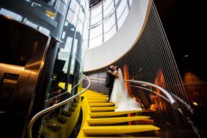 A dramatic wedding photo on yellow-lit modern stairs with curved glass architecture.