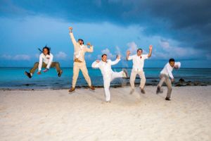 A group of people joyfully jumping on a tropical beach with blue ocean and cloudy sky in the background.