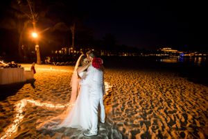 A romantic nighttime beach wedding scene illuminated by string lights with ocean waves in the background.