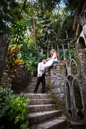 A romantic wedding scene on stone steps surrounded by lush tropical greenery and old architecture.