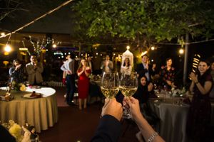 Wedding reception toast with champagne glasses raised in the foreground and party lights in background.