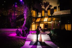 Dramatic nighttime wedding portrait with purple lighting and modern architecture.