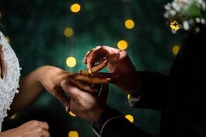 Close-up shot of wedding ring exchange with soft bokeh lights in the background.