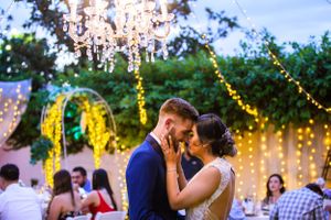 A romantic first dance under a crystal chandelier and string lights at an outdoor wedding reception.