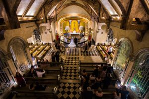 Wedding ceremony inside historic chapel with checkerboard floor and wooden beam ceiling.
