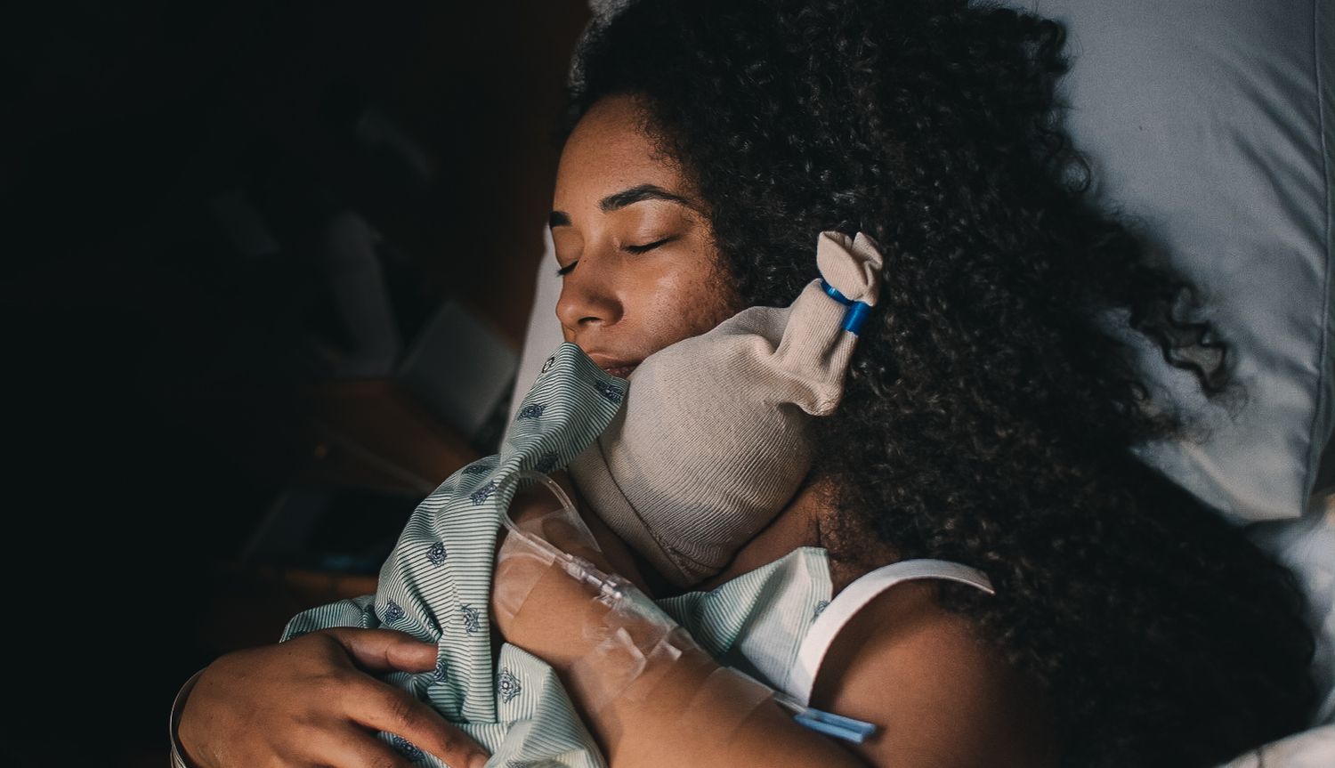 woman with eyes closed holding newborn on chest in hospital bed