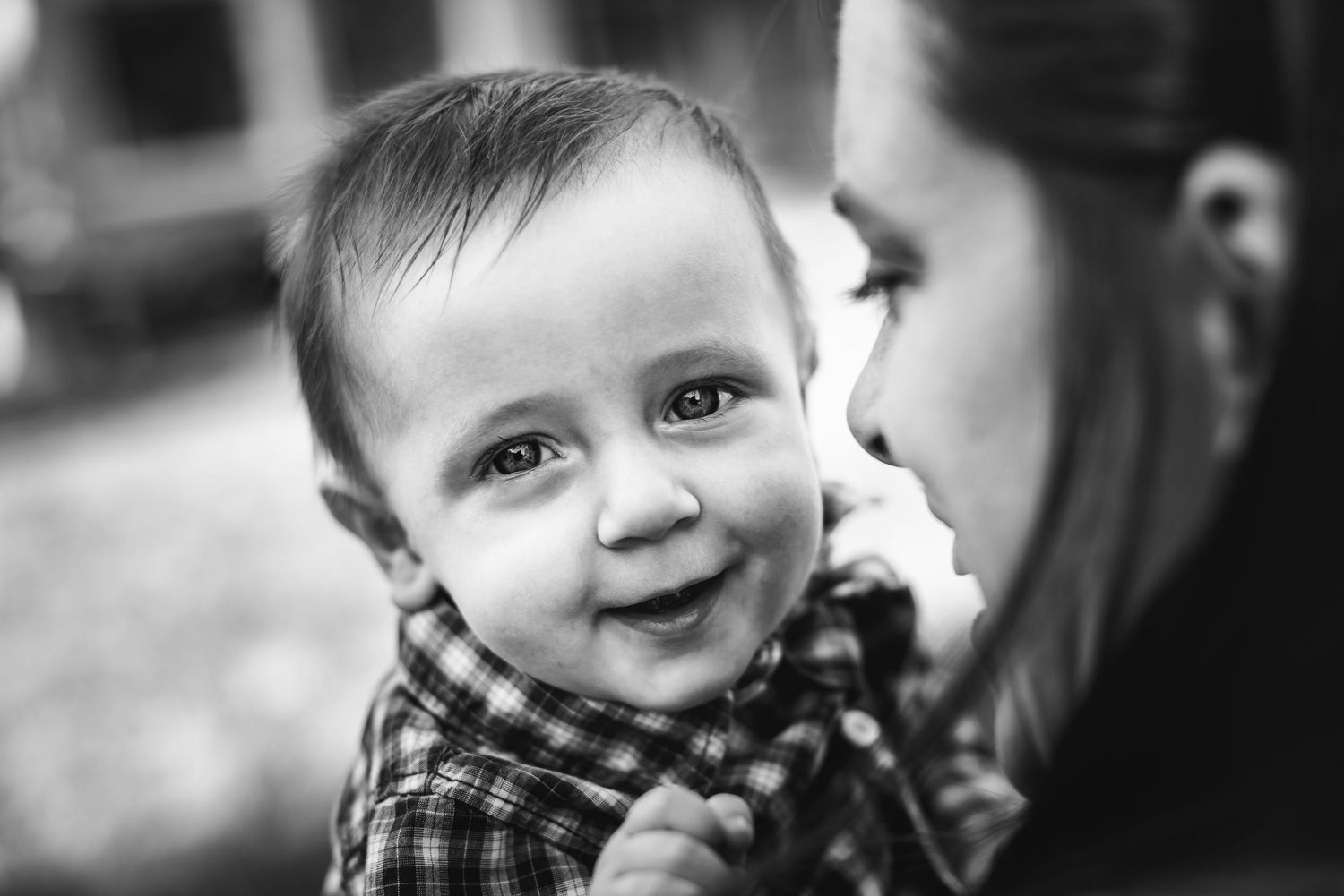 BW image of a baby boy smiling at the camera over his mother's shoulder.