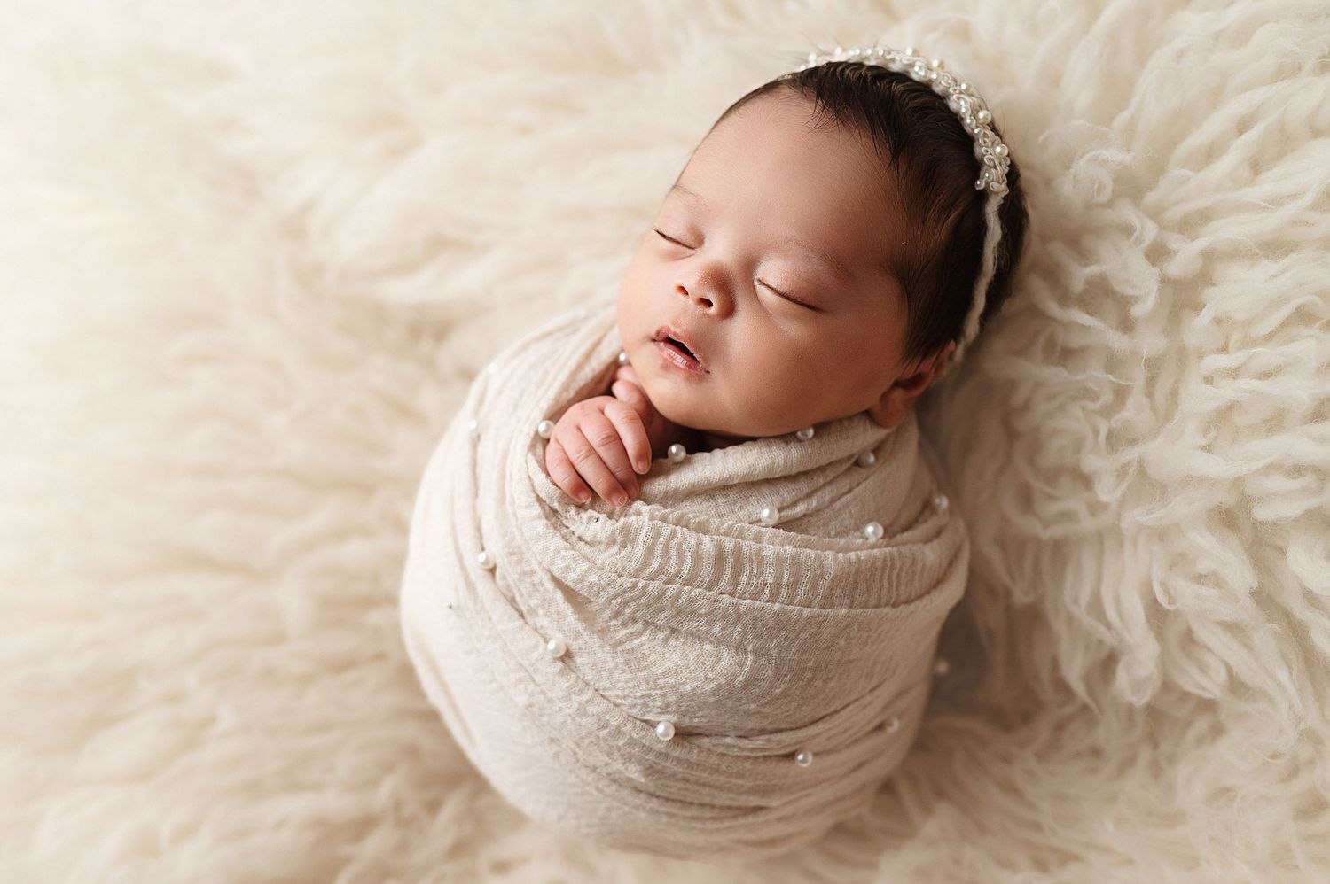 Peaceful sleeping newborn wrapped in white swaddle on soft furry backdrop.