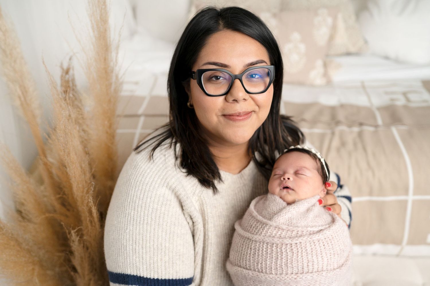 Mother in cream sweater holds newborn during professional indoor photography session.