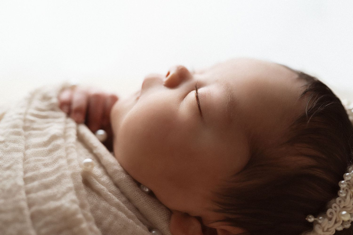 Profile view of sleeping newborn baby on white background during professional photography session.