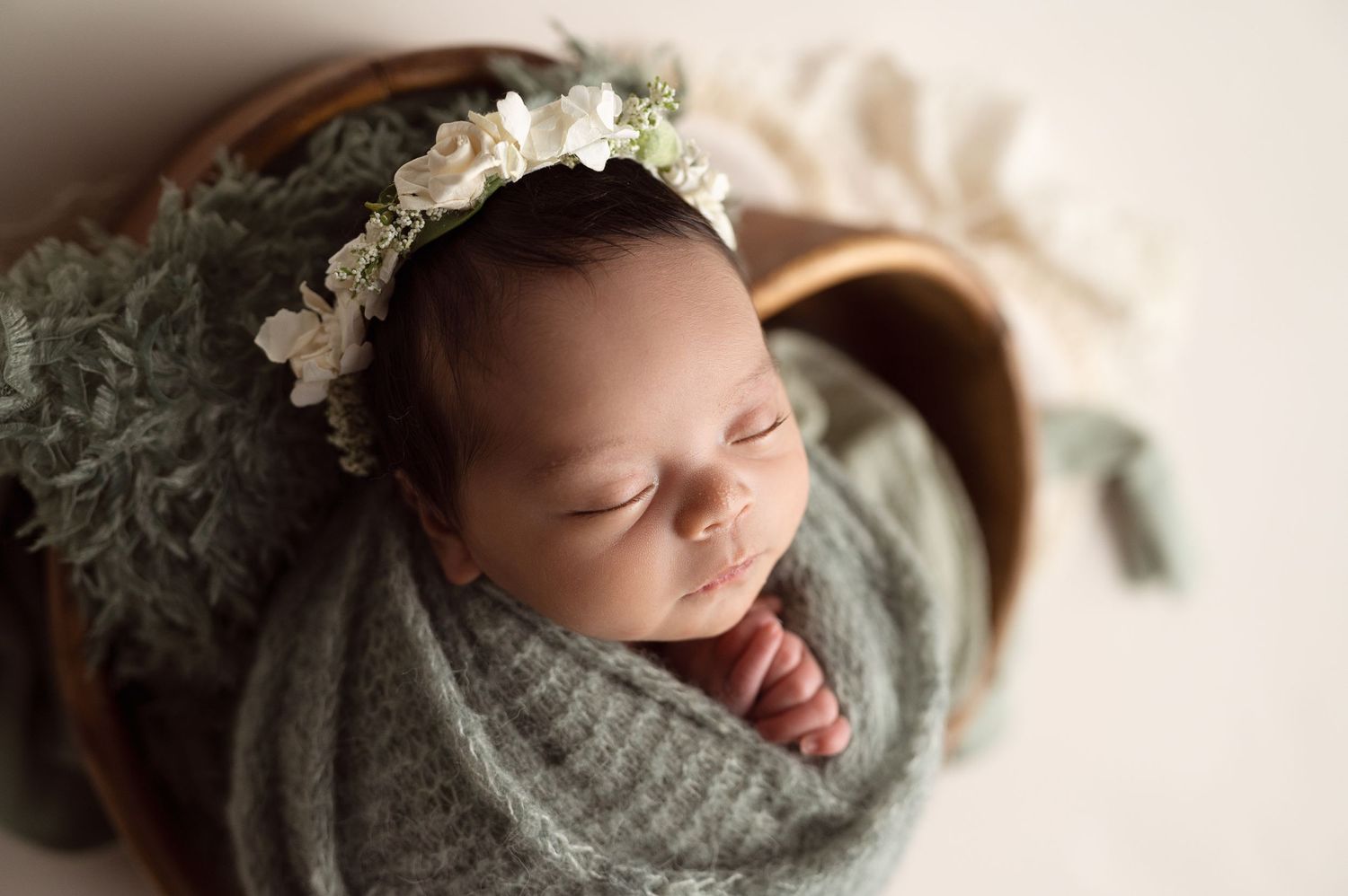 Sweet sleeping baby with floral headpiece nestled in gray swaddle.