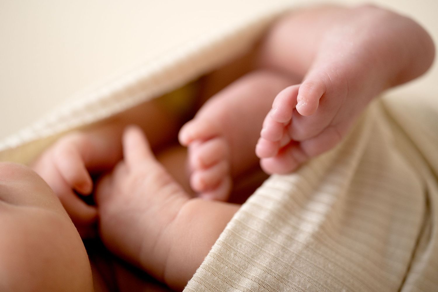 Close-up of baby's tiny feet wrapped in soft cream-colored fabric during newborn photoshoot.