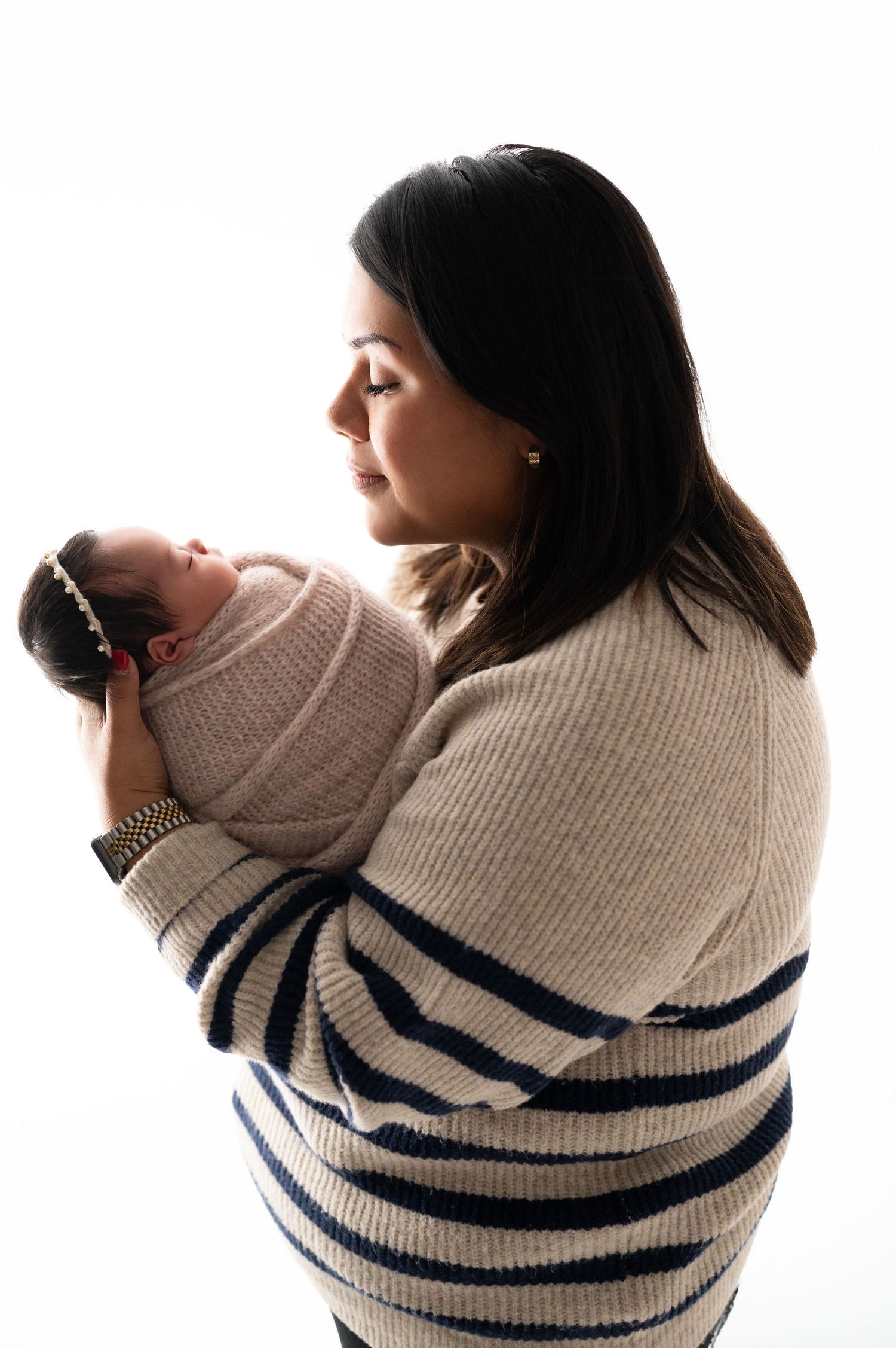 Intimate portrait of parent holding swaddled newborn in striped sweater.