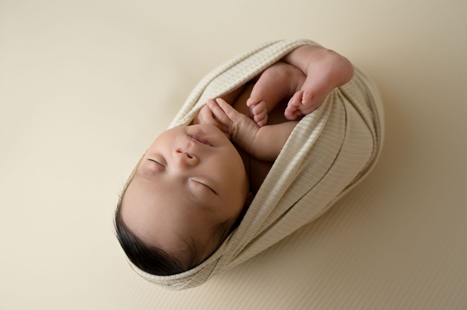 Peaceful newborn baby wrapped in cream fabric during professional portrait session.