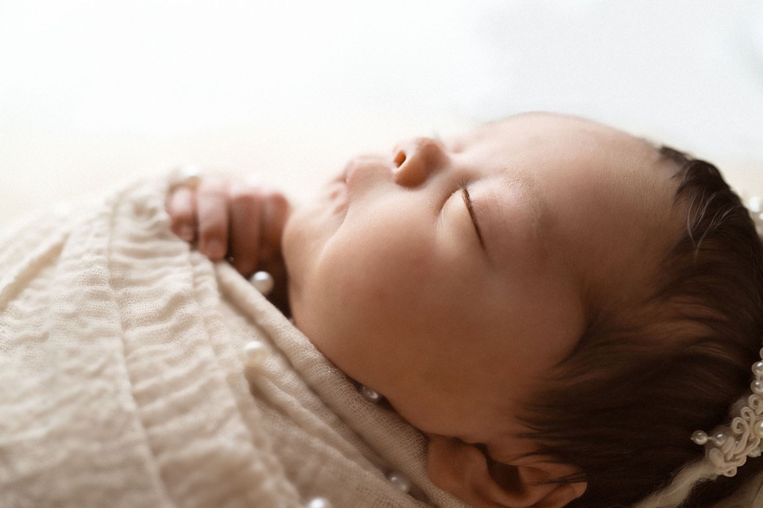 Serene close-up profile of sleeping baby wrapped in cream colored swaddle.