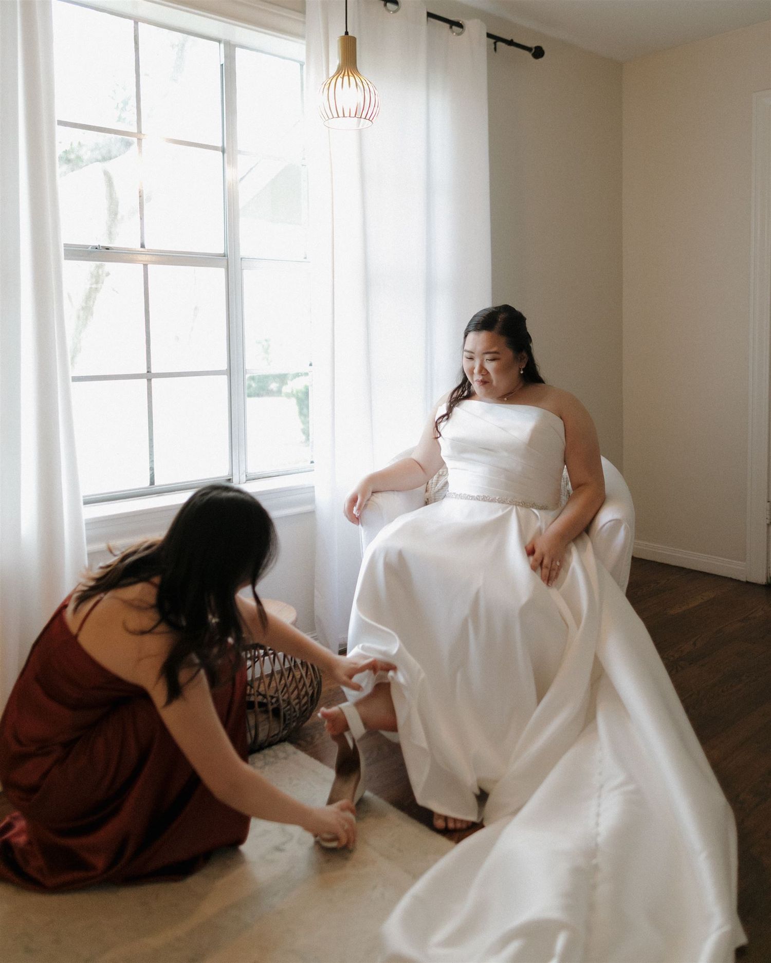 Final wedding dress preparations take place by a bright window.