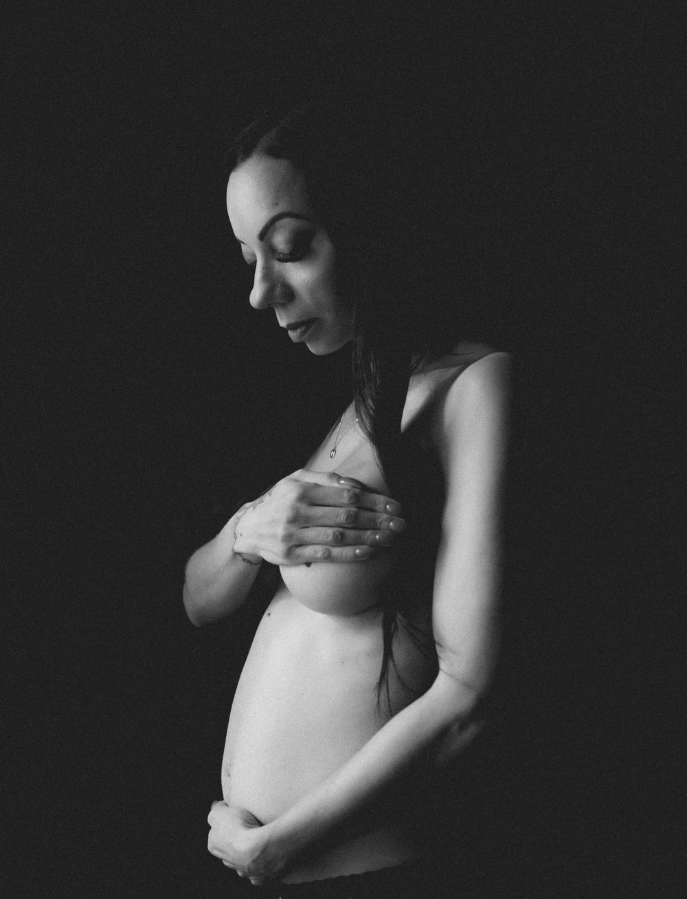 Artistic black and white maternity photography series showing silhouette against dark background.