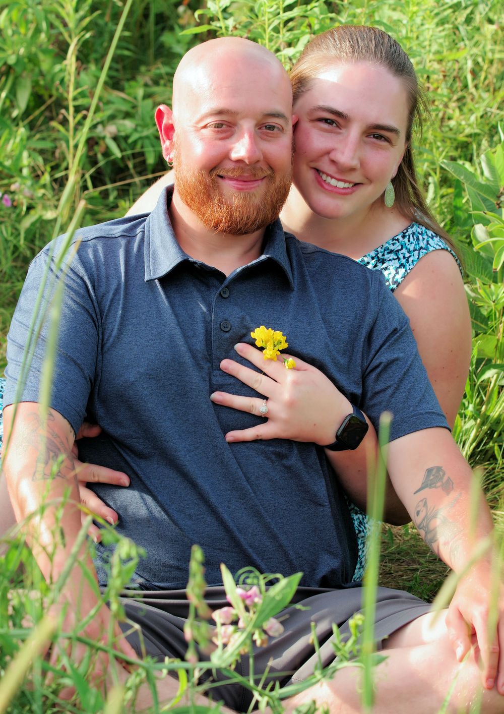 Happy couple posing with yellow flower amid lush green plants.